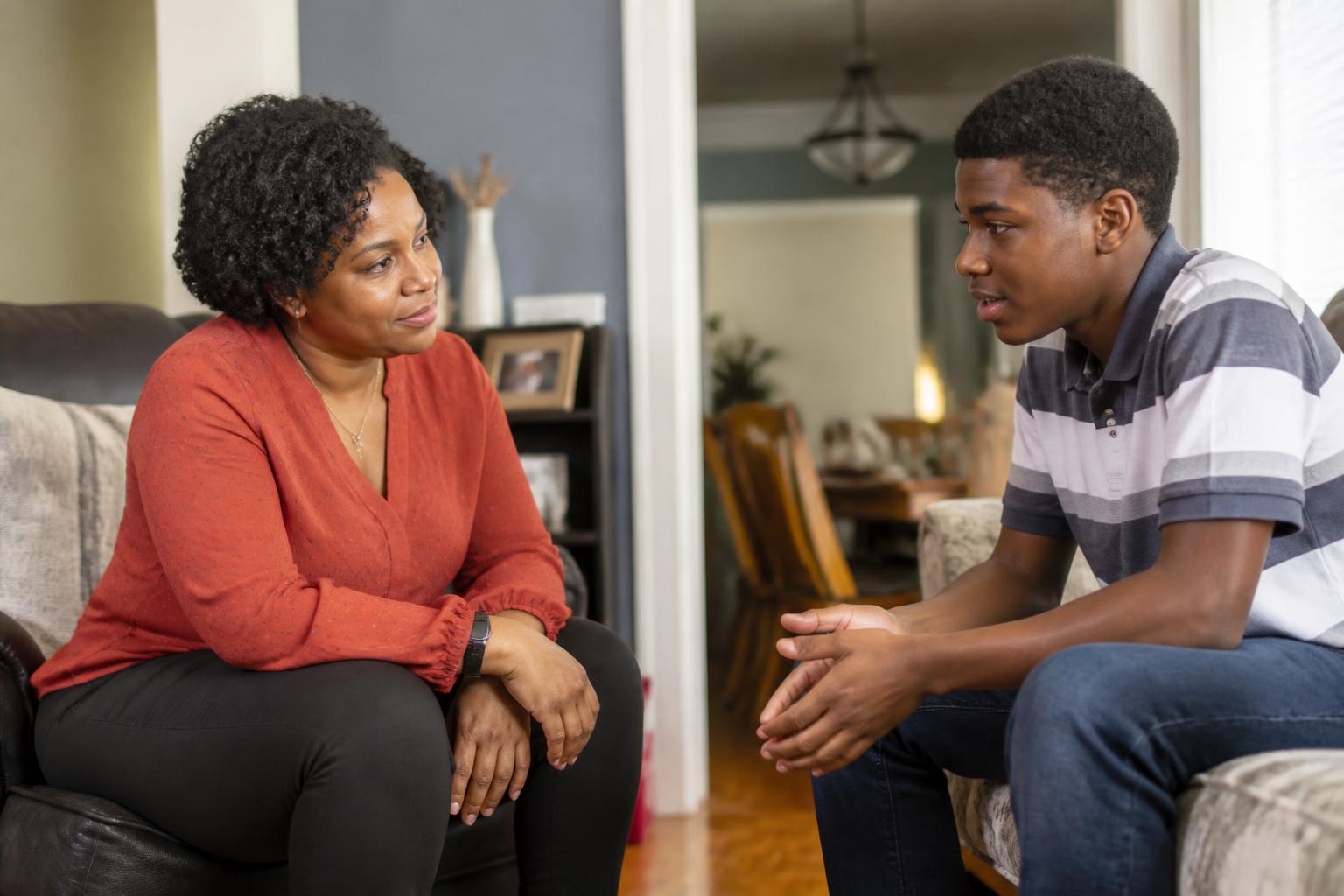 A Black mother and her young adult son sharing a warm, supportive conversation at home